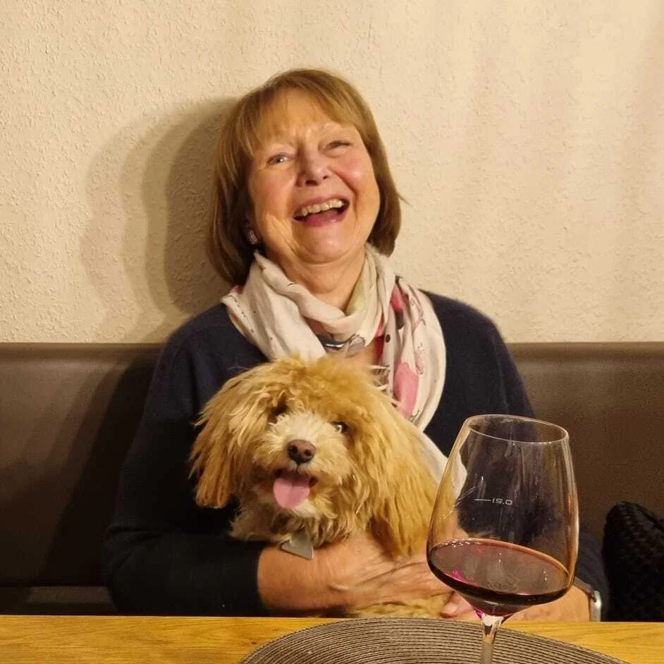 Eine Dame sitzt mit Ihrem Hund auf dem Schoß auf einer Bank im Hotel